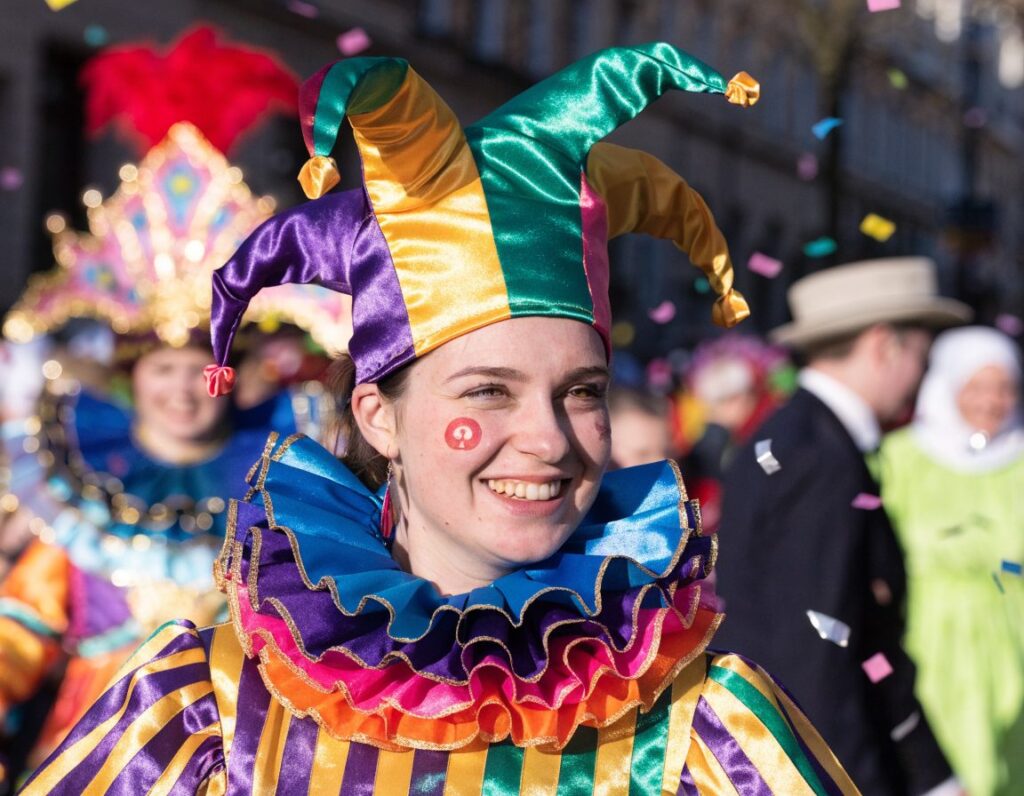 Junge Frau im Narrenkostüm mit temporärem Karneval Tattoo auf der Wange beim Umzug