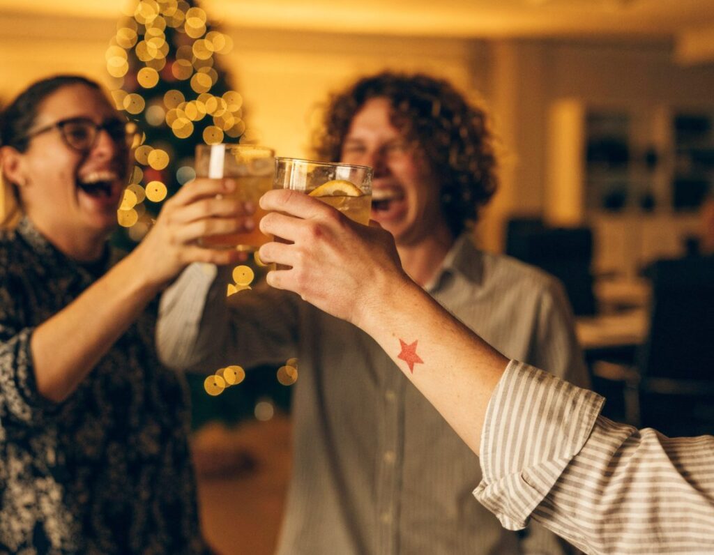 Kollegen stoßen bei der Weihnachtsfeier an, auf dem Unterarm ein temporäres Tattoo mit Firmenlogo